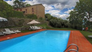 A rectangular swimming pool with a metal ladder, surrounded by red tiles. There are white lounge chairs and a stone wall with a building in the background. - Apartment in Tuscany With Stunning Hilltop Views (Pergine Valdarno)