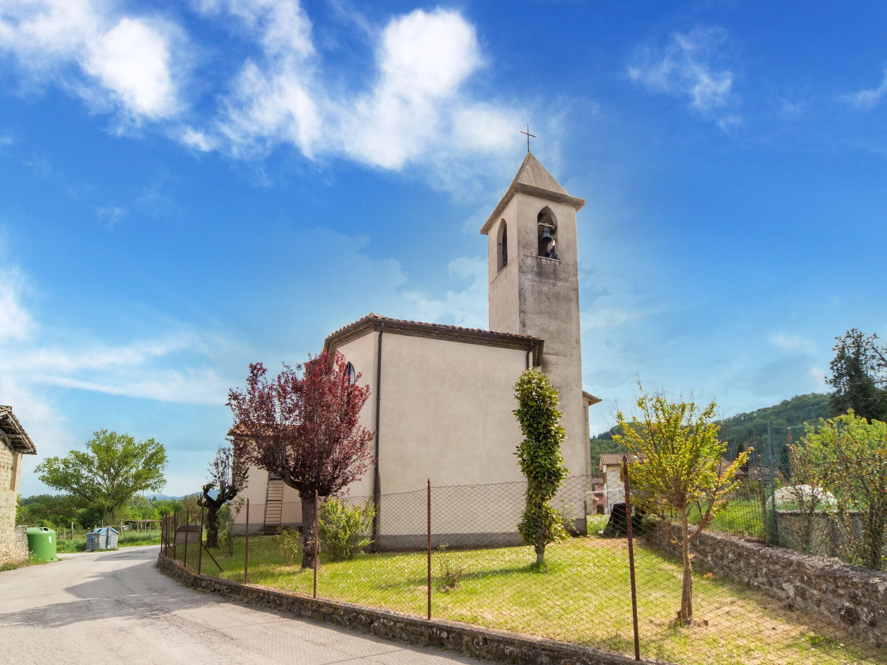 Una iglesia con un campanario, rodeada por un muro de piedra y una cerca, bajo un cielo azul despejado.