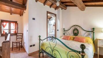 Un dormitorio con estructura de cama metálica verde, colcha amarilla y techo de madera.
