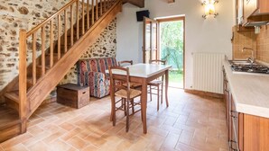 Una cocina rústica con escalera de madera, una mesa de comedor con sillas y una pared de piedra.