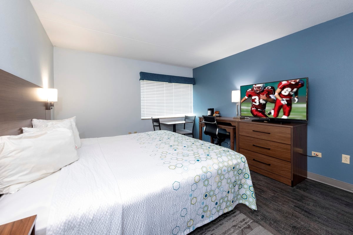 A hotel room with a bed, desk, TV, and a window with blinds.