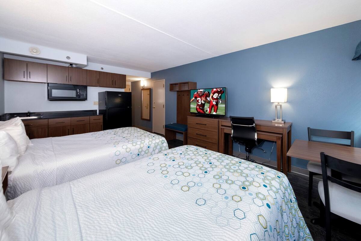 A hotel room with two beds, a desk, a television, a refrigerator, and a microwave.