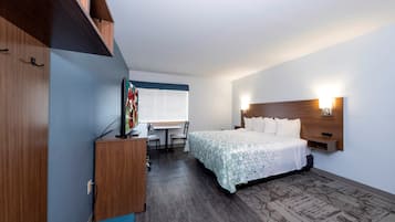 Habitación de hotel con cama, escritorio, silla, televisor y ventana con persianas.