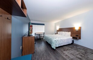 Habitación de hotel con cama, escritorio, silla, televisor y ventana con persianas.