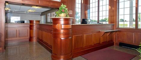 A reception area with a wooden reception desk, a potted plant, and a view of the outdoors through large windows.