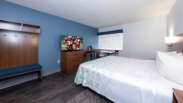A hotel room with a bed, a desk with a chair, a wardrobe, and a painting on the wall.