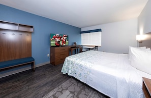 A hotel room with a bed, a desk with a chair, a wardrobe, and a painting on the wall. - HomeTowne Studios by Red Roof Wilmington - New Castle (New Castle)