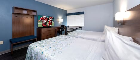 A hotel room with two beds, a desk with a chair, a TV, and a window with blinds.