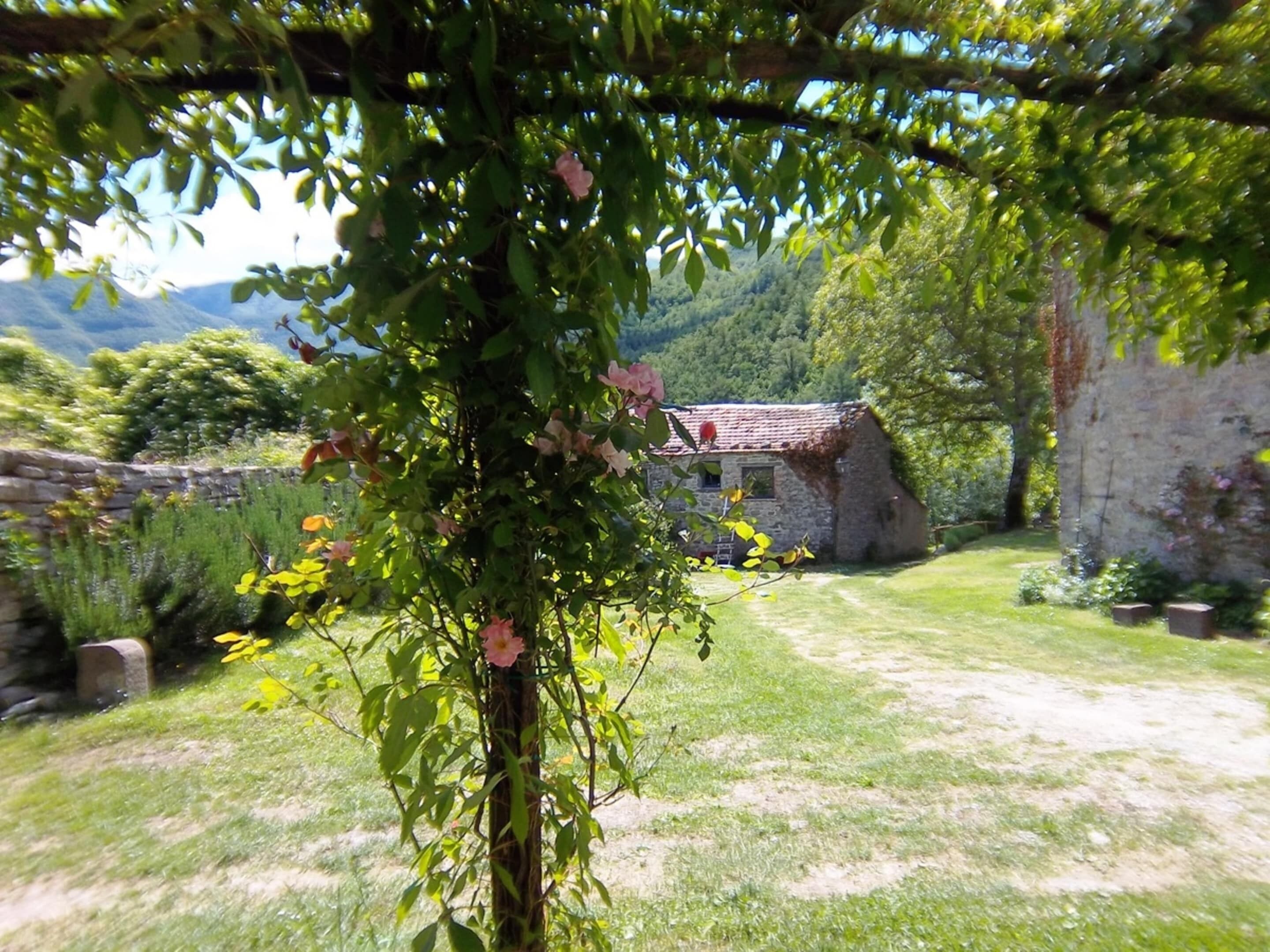 A stone building with a red-tiled roof, surrounded by a grassy area and a stone wall.