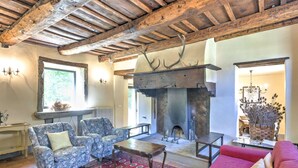 A rustic living room with exposed wooden beams, a fireplace, floral armchairs, a red sofa, and a patterned rug. - Comfortable Home in San Godenzo near Lake (San Godenzo)