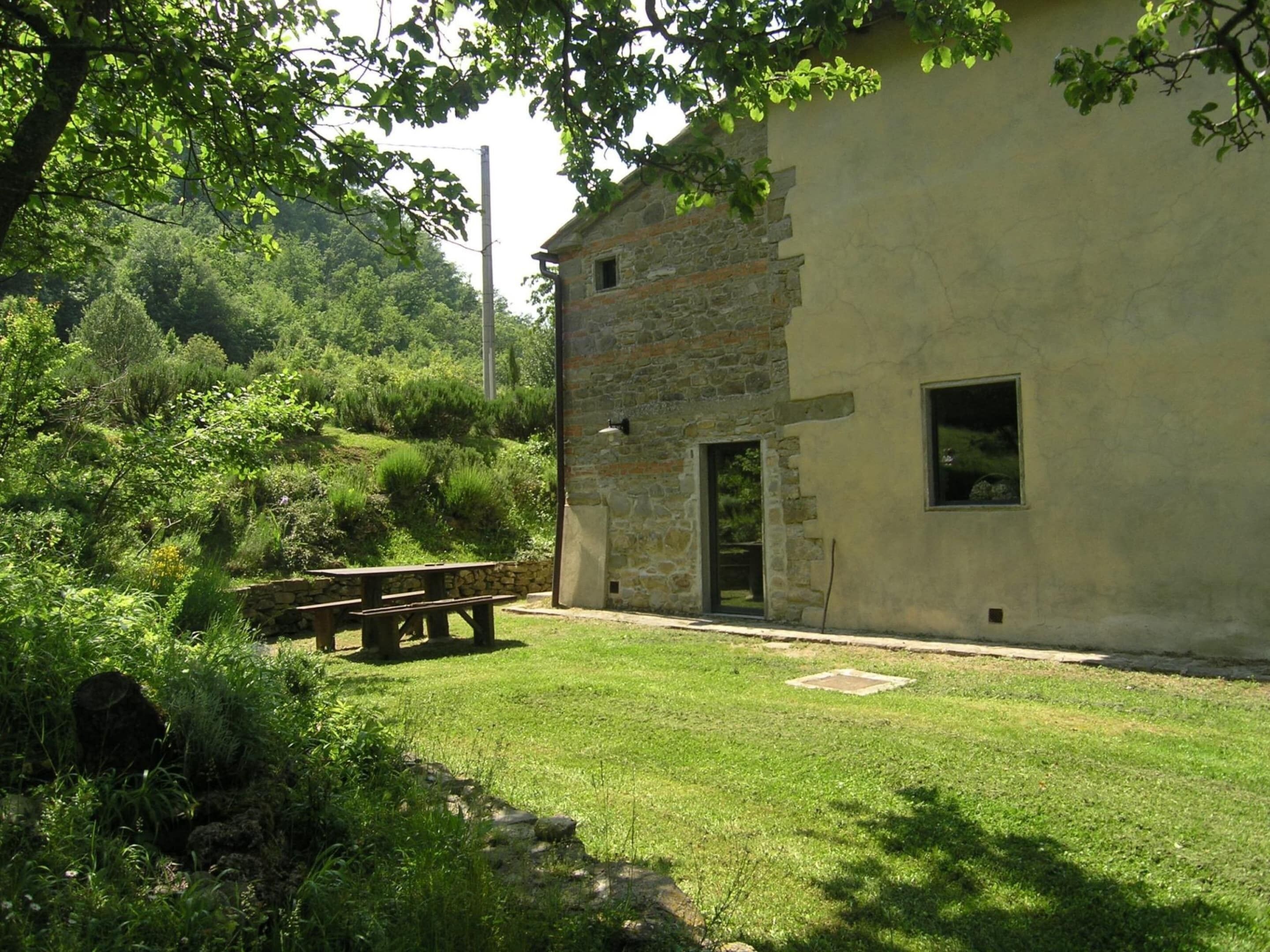 A rustic stone building with a grassy yard, a wooden bench, and a stone wall.