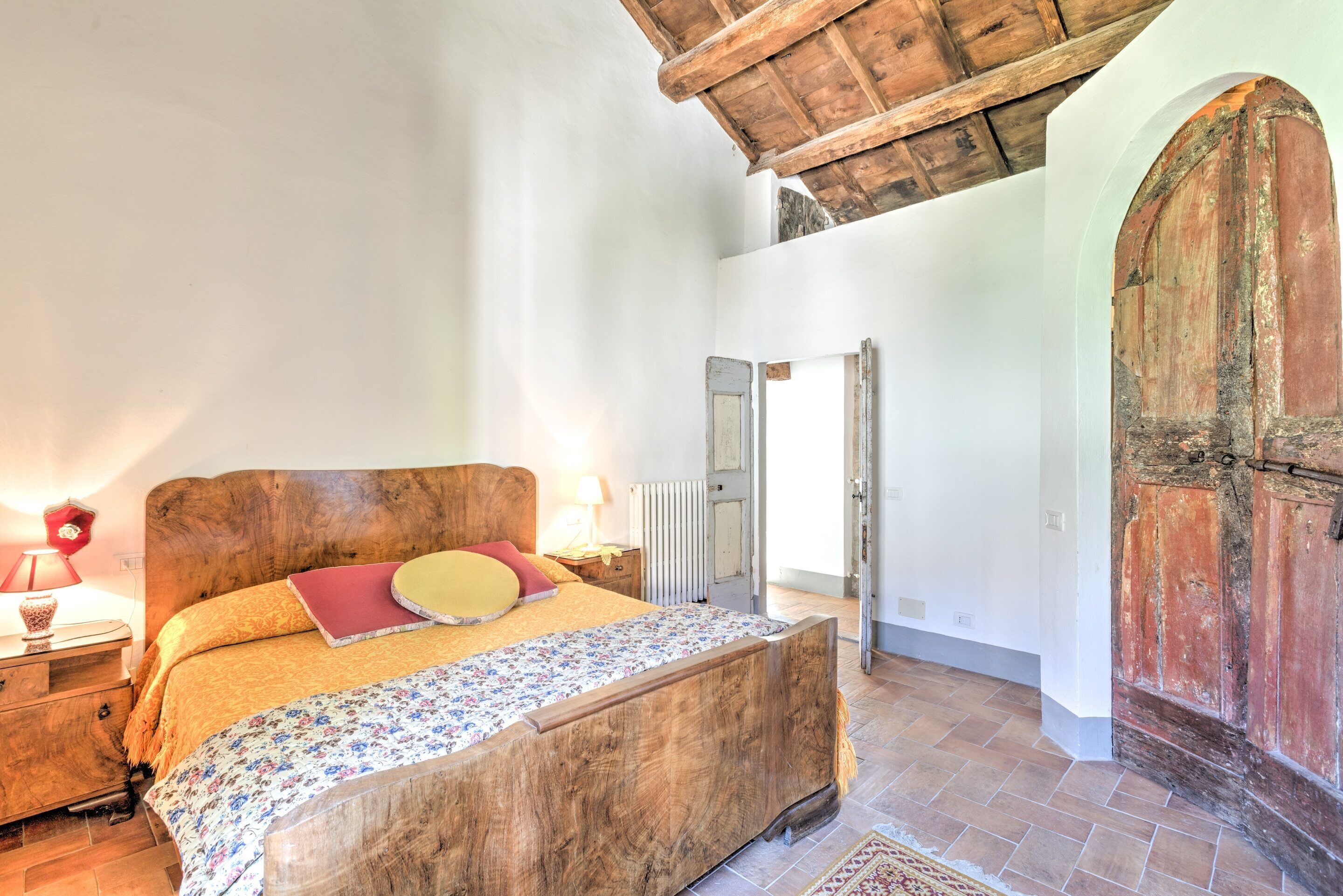 A bedroom with a wooden bed, a nightstand, a lamp, and a large wooden door.