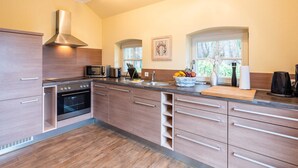 A modern kitchen with a built-in oven, stainless steel range hood, and a large window providing natural light. - Ferienhaus Silbermöwe - Haus Silbermöwe (Loddin)