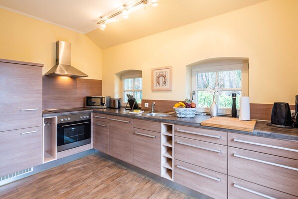 A modern kitchen with a built-in oven, stainless steel range hood, and a large window providing natural light.