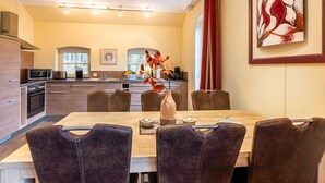 A modern kitchen with a dining area, featuring a wooden table, dark chairs, and a vase with autumn leaves. - Ferienhaus Silbermöwe - Haus Silbermöwe (Loddin)