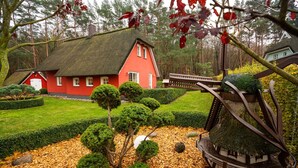 A red house with a thatched roof surrounded by a well-maintained garden with hedges and a decorative metal structure. - Ferienhaus Silbermöwe - Haus Silbermöwe (Loddin)