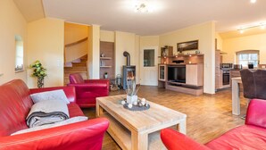 A spacious living area with a wooden coffee table, red leather sofas, a TV, and a kitchen in the background. - Ferienhaus Silbermöwe - Haus Silbermöwe (Loddin)