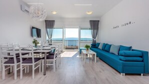 Ein modernes Wohnzimmer mit einem blauen Sofa, einem Esstisch mit Stühlen und einem großen Fenster mit Vorhängen.