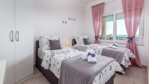 Ein Hotelzimmer mit zwei Betten, einem Kleiderschrank, einem Fenster mit rosa Vorhängen und Meerblick.
