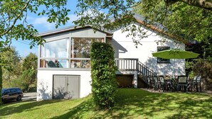 Une maison moderne à deux étages, dotée d’un grand garage, d’un espace extérieur aménagé avec un coin salon couvert et d’une pelouse bien entretenue.