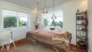 Une pièce comprenant un lit, une petite table, une étagère avec des livres et une fen être avec des stores.