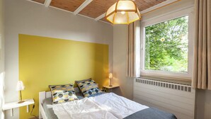 Une chambre à coucher avec un lit, une table de chevet avec une lampe, une fenêtre avec des rideaux et un plafond en bois.