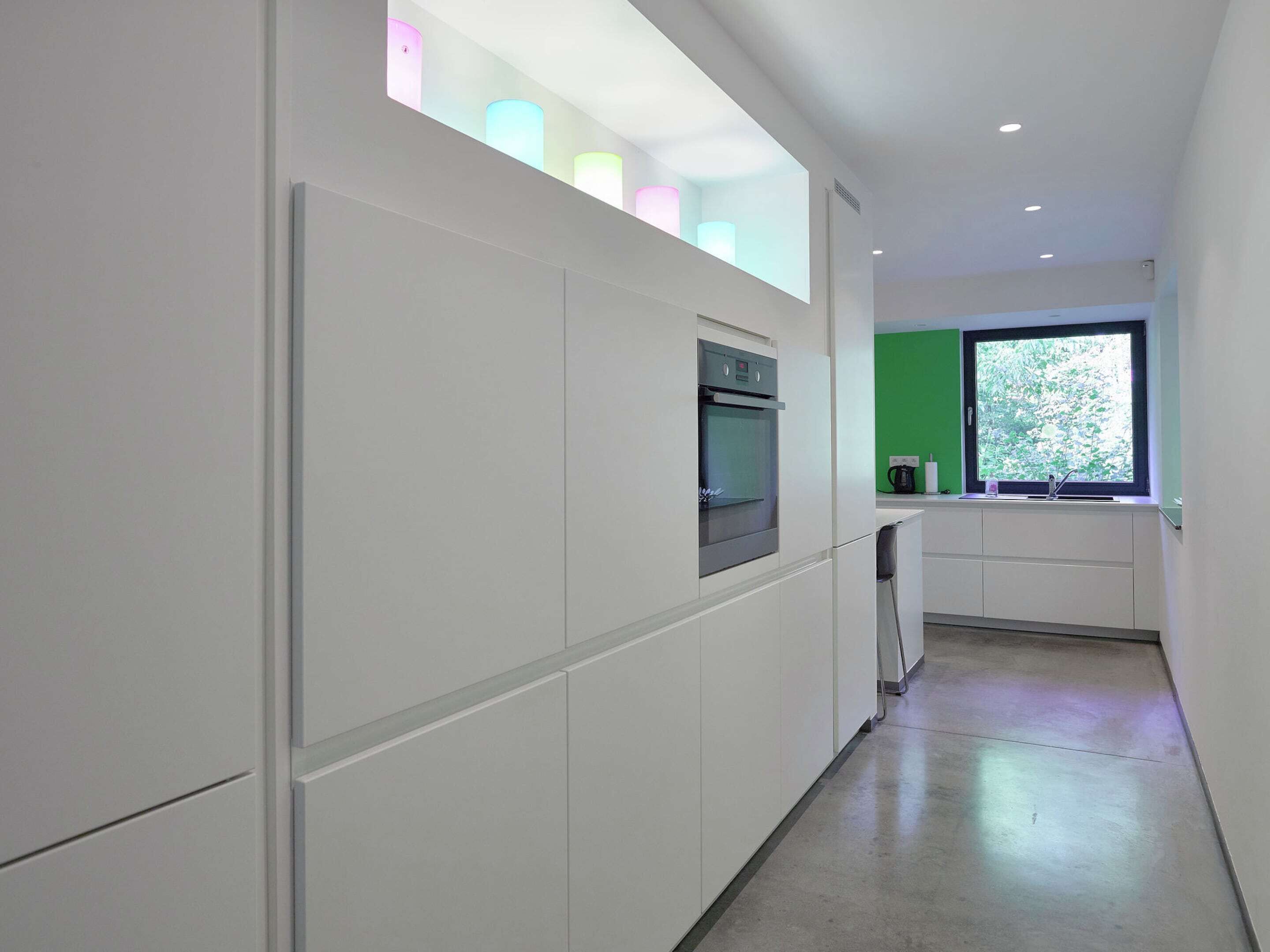 A modern kitchen with white cabinetry, a built-in oven, and a window with a view of greenery.