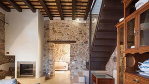 Una sala de estar acogedora con pared de piedra, chimenea, escalera de madera y un mueble con puertas de cristal.