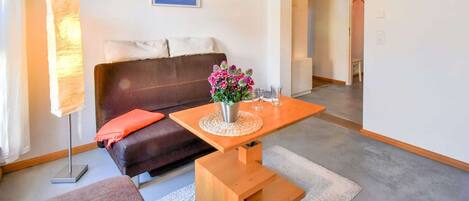 A modern living room with a brown leather sofa, a wooden coffee table with a vase of flowers, a floor lamp, and a framed quote on the wall.