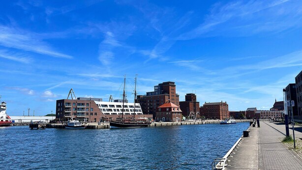 A waterfront cityscape with a historic building, a modern structure, and a traditional boat docked at the pier. - Frisch Renovierte Wohnung im Zentrum von Wismar (Wismar)