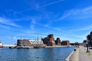 A waterfront cityscape with a historic building, a modern structure, and a traditional boat docked at the pier. - Frisch Renovierte Wohnung im Zentrum von Wismar (Wismar)