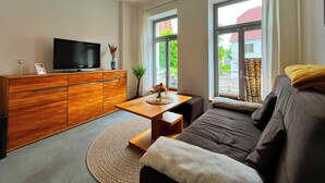 A modern living room with a sofa, a coffee table, a TV on a wooden cabinet, and large windows. - Frisch Renovierte Wohnung im Zentrum von Wismar (Wismar)