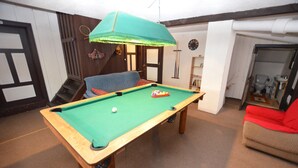 Una mesa de billar con superficie de fieltro verde, una bola rayada roja y blanca, y una bola blanca. Hay un sillón azul y un sillón rojo en la habitación.