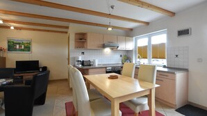 A modern kitchen with wooden beams, a dining area with a table and chairs, and a TV in the living area. - Wohnung in Stellshagen, Niklas (Damshagen)
