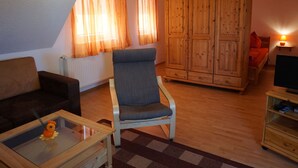 A living room with a sofa, armchair, wooden cabinet, and a TV stand. - Wohnung mit Garten in Wieck a. Darss (Wieck auf dem Darss)