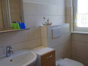 A bathroom with a sink, toilet, and a small shelf with a ship model. - Wohnung mit Garten in Wieck a. Darss (Wieck auf dem Darss)