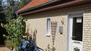 A brick house with a white door, a small garden with potted plants, and blue plastic chairs. - Wohnung mit Garten in Wieck a. Darss (Wieck auf dem Darss)