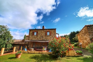 A stone building with a tiled roof, a covered outdoor seating area, and a garden with red flowers. - Scenic Tuscan Farmhouse (Castiglione d'Orcia)