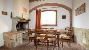 A dining area with a stone fireplace, wooden chairs, and a brick archway.