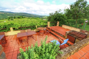 A patio with a wooden table and chairs, a blue chair, and a grill. - Scenic Tuscan Farmhouse (Castiglione d'Orcia)