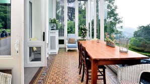 A dining area with a wooden table and chairs, a patterned rug, and a view of greenery through large windows. - Spacious Pet-friendly Castle in Stavelot (Stavelot)