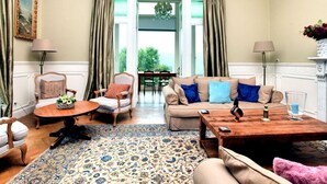 A spacious living room with a large window, a wooden coffee table, a beige sofa, and a patterned rug. - Spacious Pet-friendly Castle in Stavelot (Stavelot)