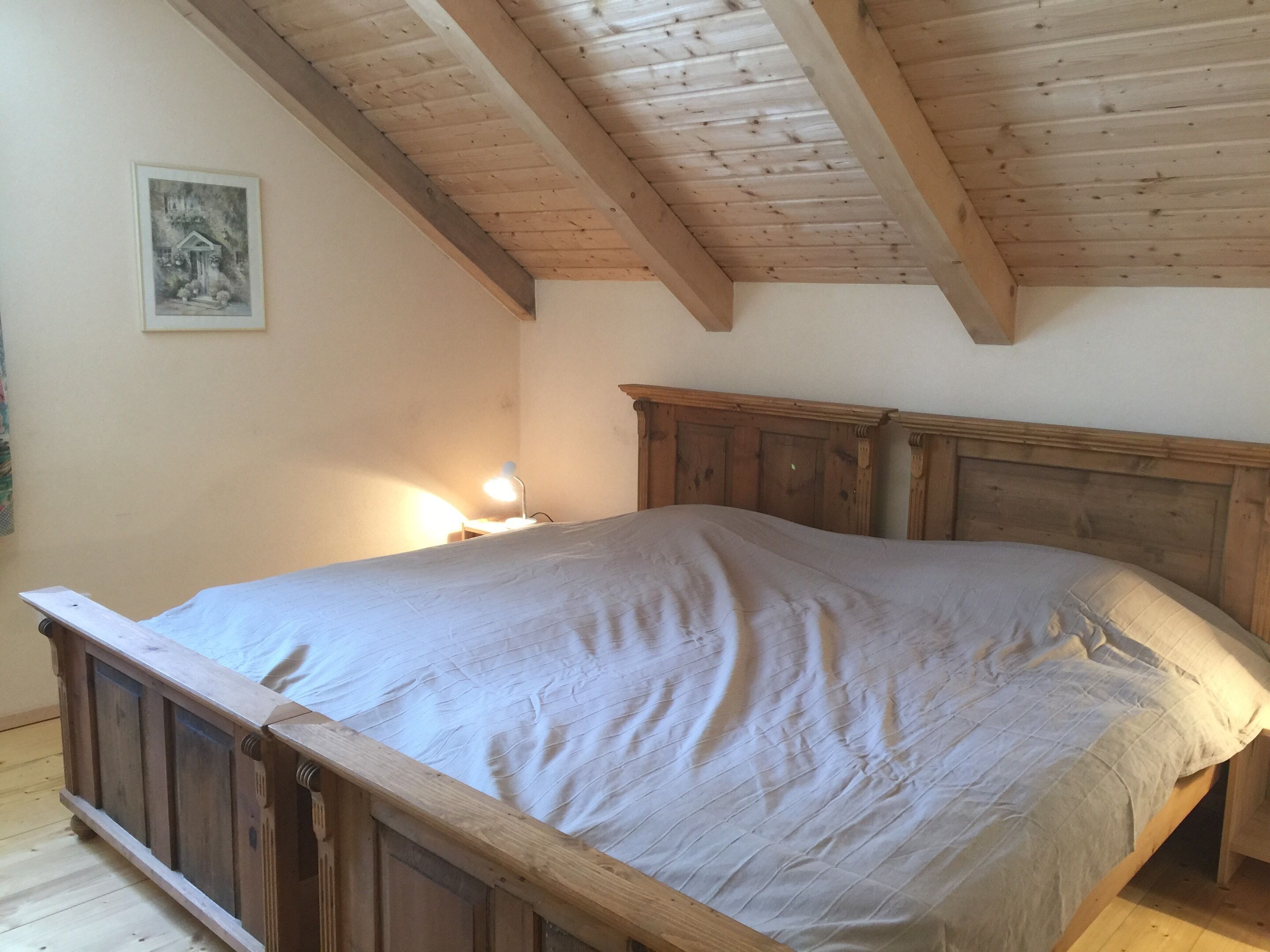 A bedroom with a wooden bed frame, a headboard, and a nightstand with a lamp.