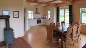 Una cocina amplia con vigas de madera, una mesa de comedor con sillas de mimbre y un gran ventanal con vistas a la vegetación.