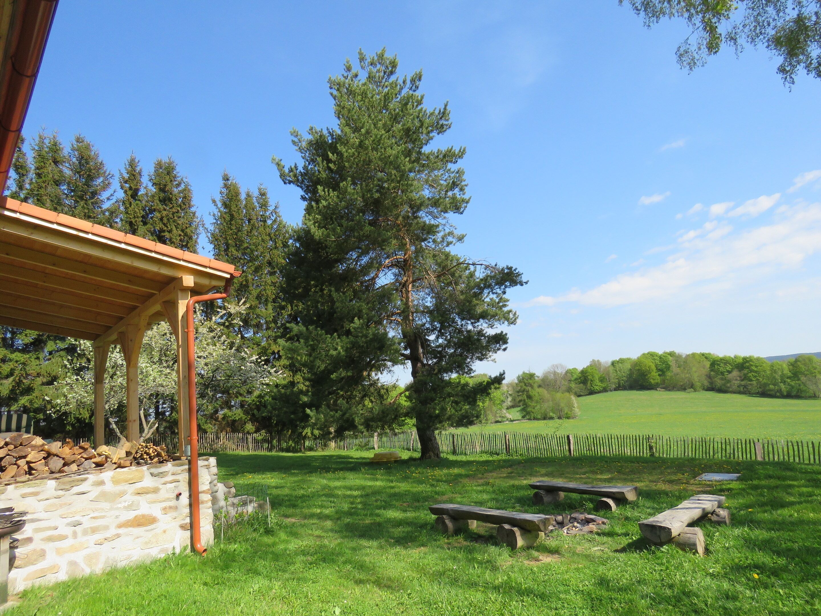 A rustic outdoor area with a stone wall, wooden benches, and a pergola.