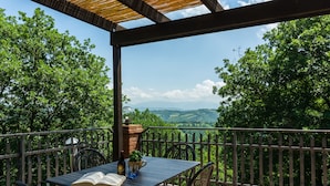 A covered outdoor patio with a table, chairs, and a view of the countryside. - Belvilla by Oyo Azalea in Gubbio (Gubbio)