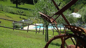 A rustic outdoor setting with a large metal wheel structure, a wooden fence, and a swimming pool in the background. - Belvilla by Oyo Azalea in Gubbio (Gubbio)