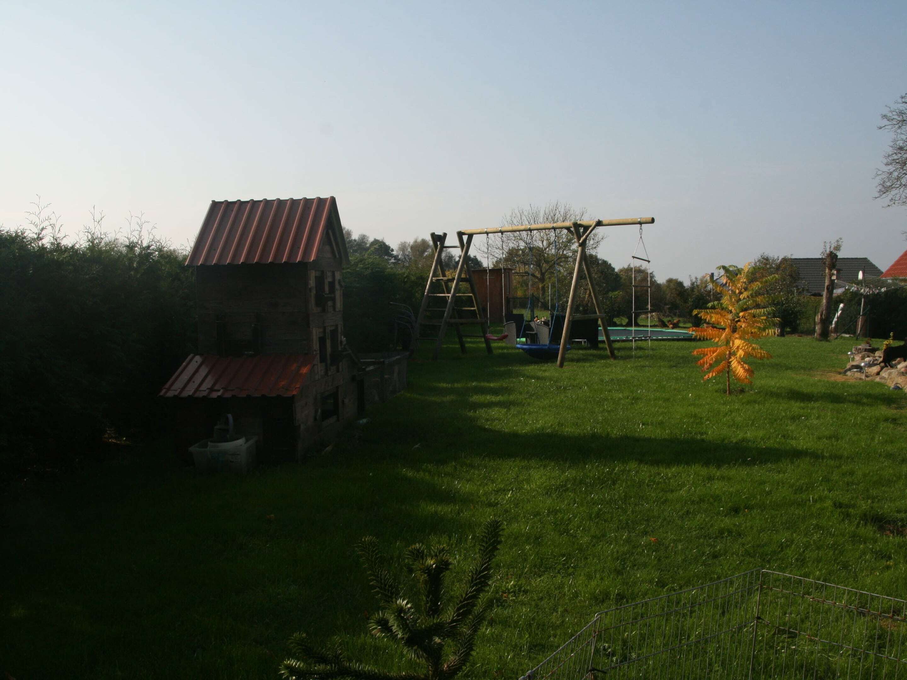 A rustic wooden house with a red roof, a swing set, and a fenced yard.