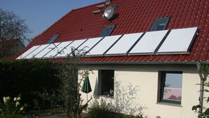 A house with a red tiled roof, a white exterior, and a garden with a patio area. - Cozy Apartment in Kägsdorf near Sea (Bastorf)