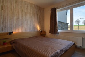 Une chambre à coucher avec une tête de lit en bois, un lit recouvert d’une couverture marron, une table de chevet avec une lampe et une fenêtre avec des rideaux.